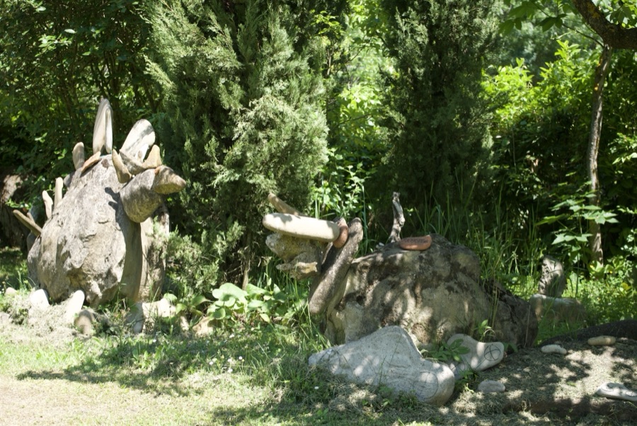 Due stegosauri di sasso con piastre e corna, affiancati davanti a una fila di cipressi