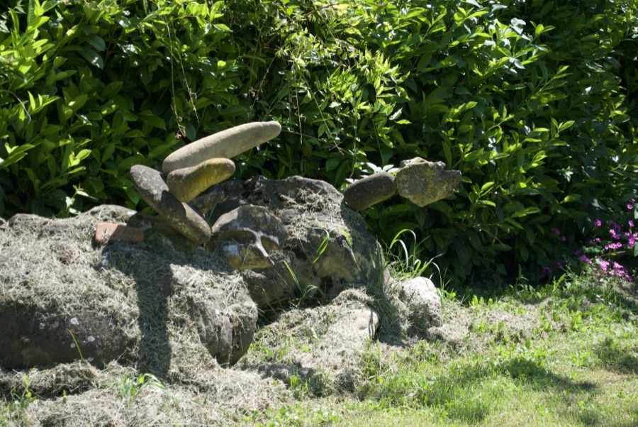 Dettaglio di zampe di sasso decorate con frammenti di coccio, in pieno sole tra i fiori di glicine