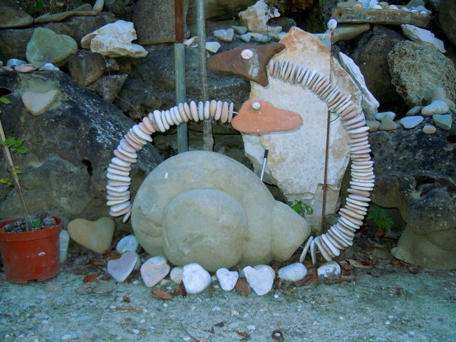Scultura antropomorfa di pietra con occhi bianchi e arancioni, accanto a un sasso dipinto con una scritta