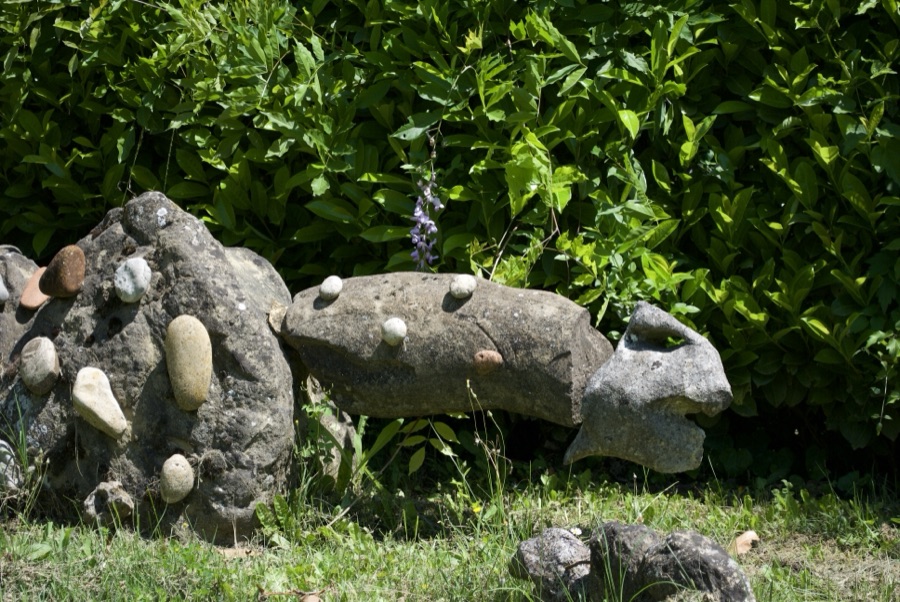 Scultura a forma di lucertola tempestata di piccoli sassolini colorati, in pieno sole