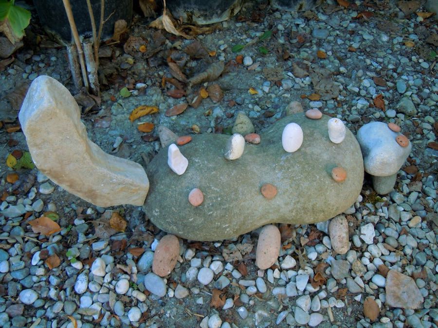 Scultura a forma di lucertola con spuntoni di ciottoli colorati sulla schiena