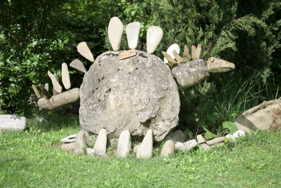 Angolo del giardino con panchina rossa e cartello TRACCE DEL PASSATO tra sculture di sasso