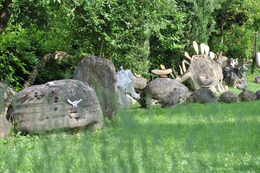 Vista panoramica del giardino con diverse sculture di dinosauro tra il prato e gli alberi