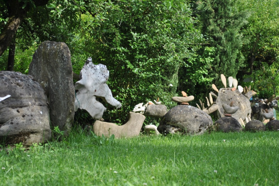 Panoramica di una fila di sculture di sasso, con teschi bianchi e un lungo collo a ciottoli in primo piano