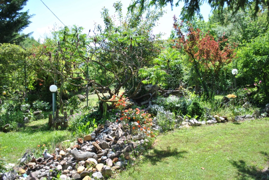 Veduta del giardino con un ruscello di ciottoli bianchi, fiori arancioni e alberi in fiore