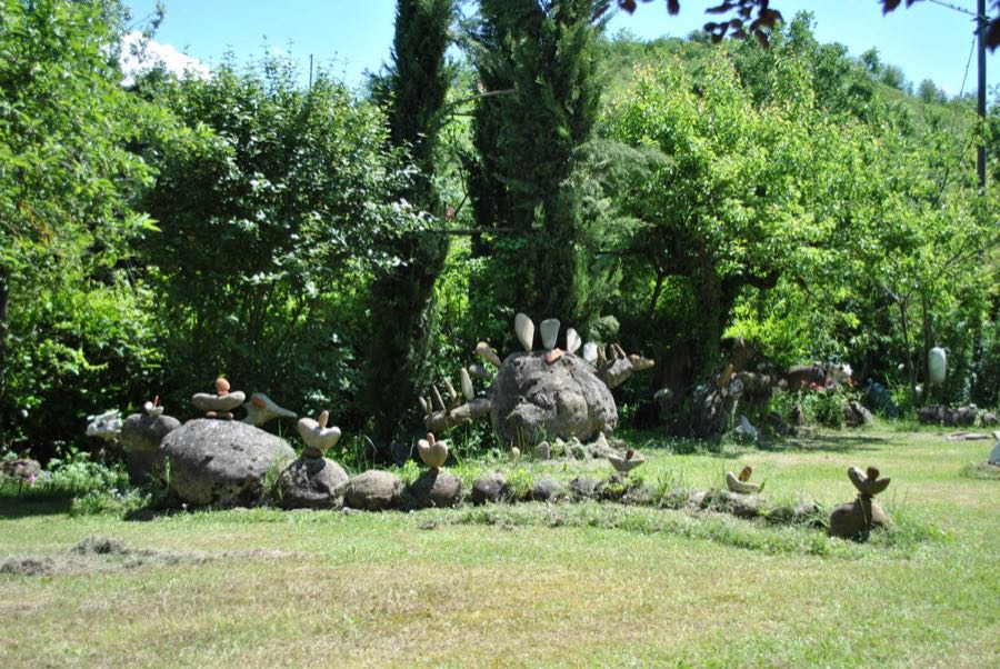 Stegosauro di pietra con piastre triangolari sulla schiena, tra i cipressi del giardino