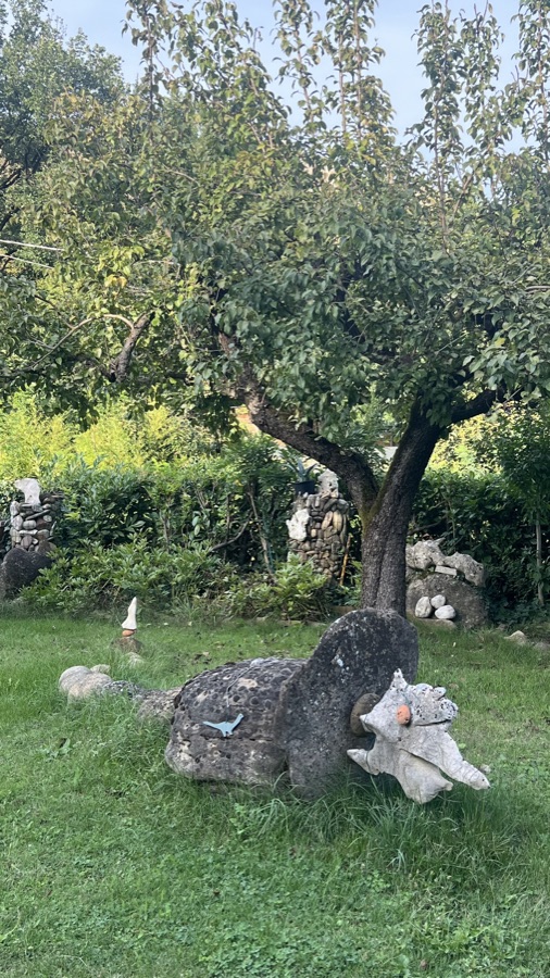 Teschio di sasso a forma di uccellino con una targhetta metallica a forma di dinosauro, sotto un albero
