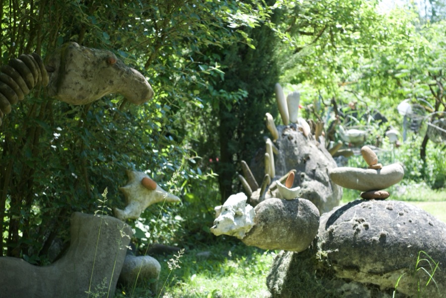 Testa di dinosauro di sasso con dettagli in ceramica colorata, tra sculture e sassi impilati in equilibrio