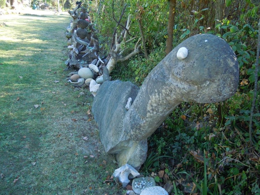 Testa di dinosauro di pietra con occhio di ciottolo, vicino a un sasso con scritto UOVA DI DINOSAURO